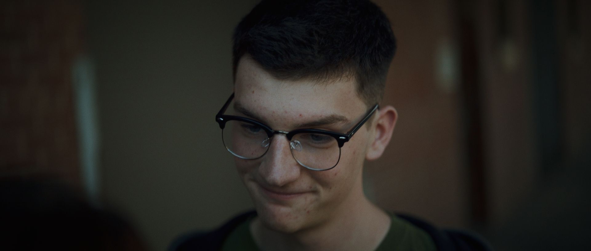 Still from Give It Up: a young man in glasses fights back a smile