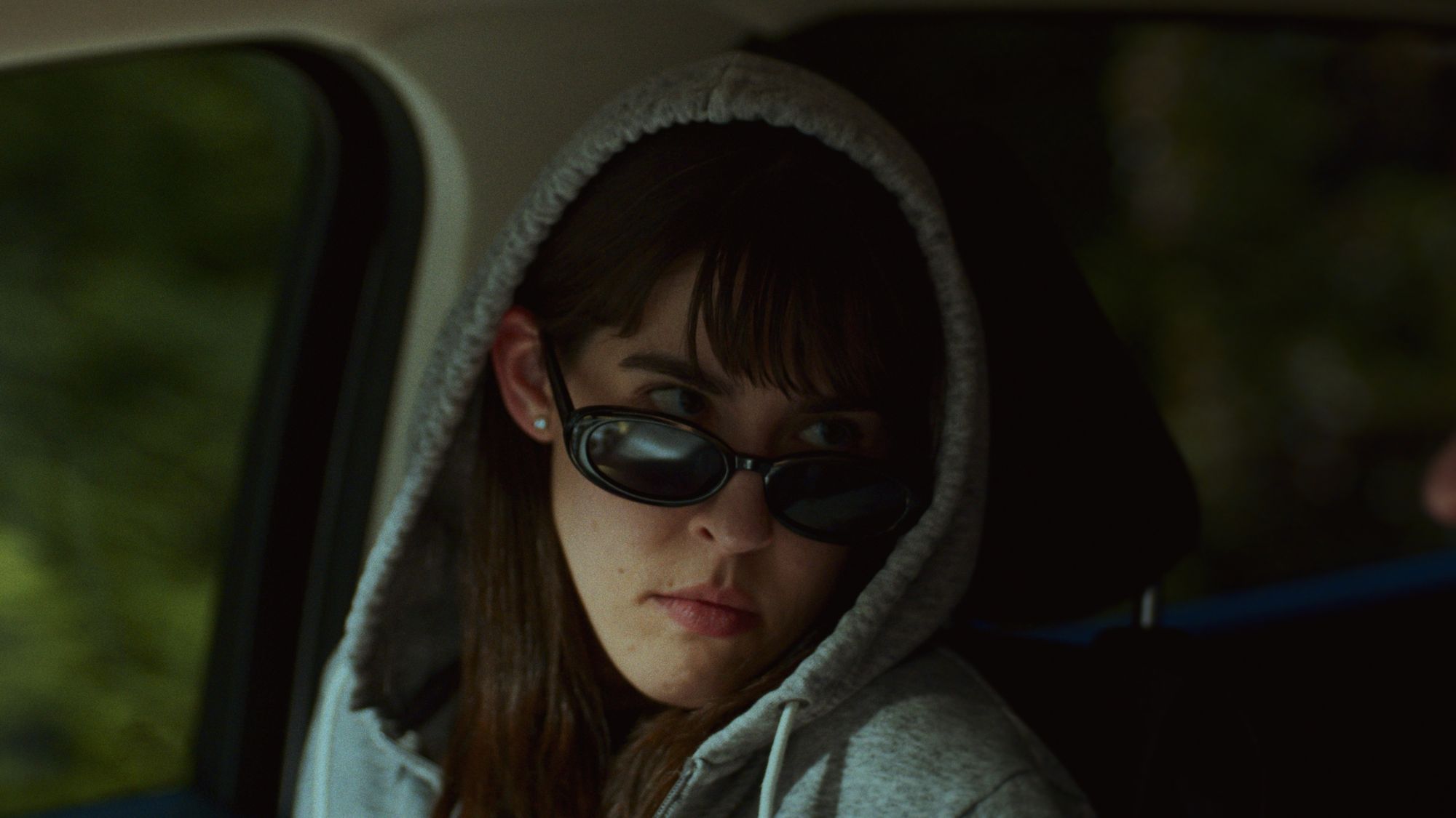 Still from The Following: a woman in a hoodie and sunglasses keeps watch from a car