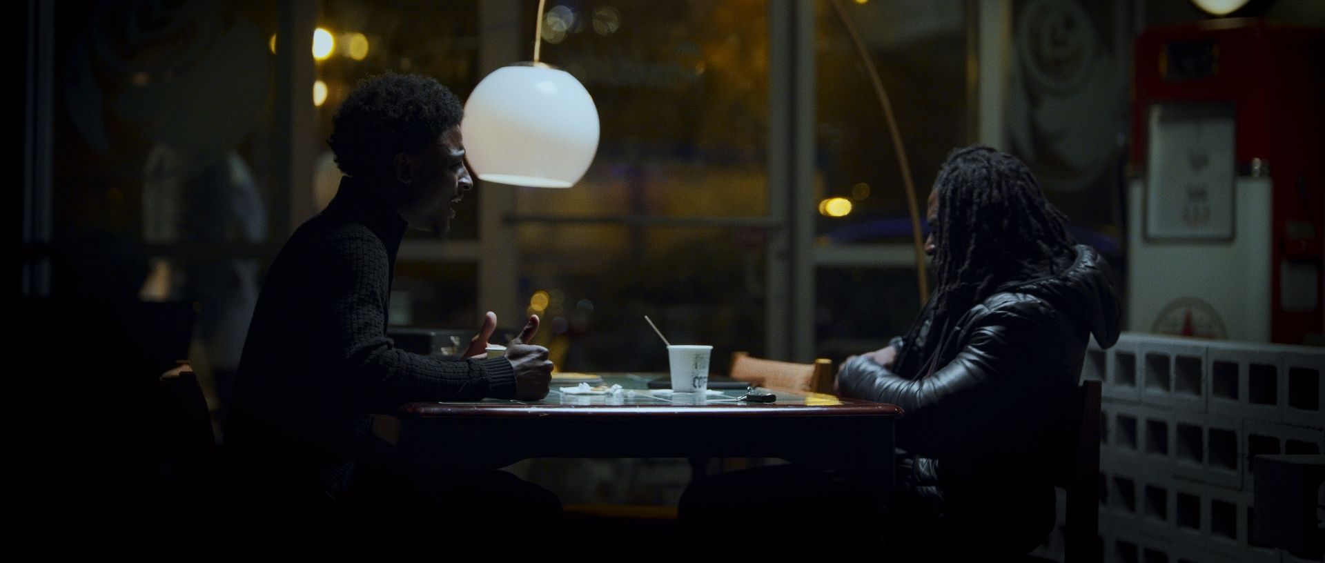 Still from The Order: two men face off across a diner table at night